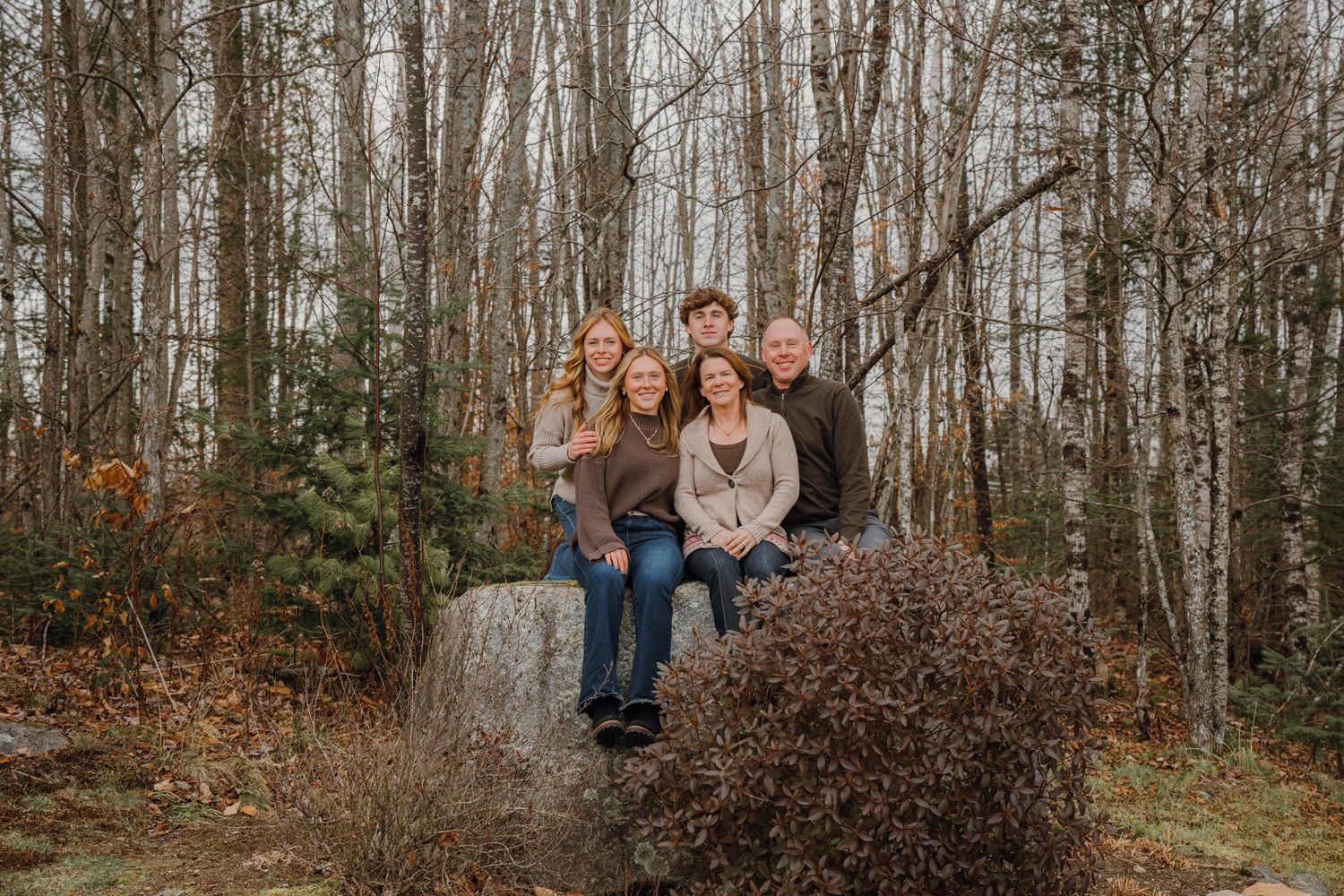 Family of five poses on a large rock surrounded by bare birch trees in a woodland setting.