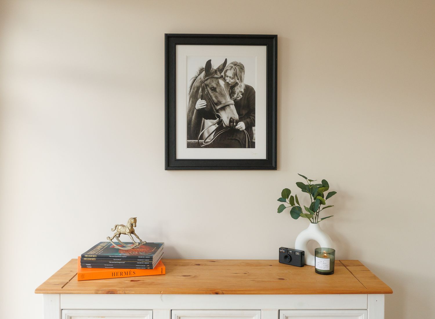 A minimalist gallery wall with black and white framed photographs above a white sideboard with plants and decor.