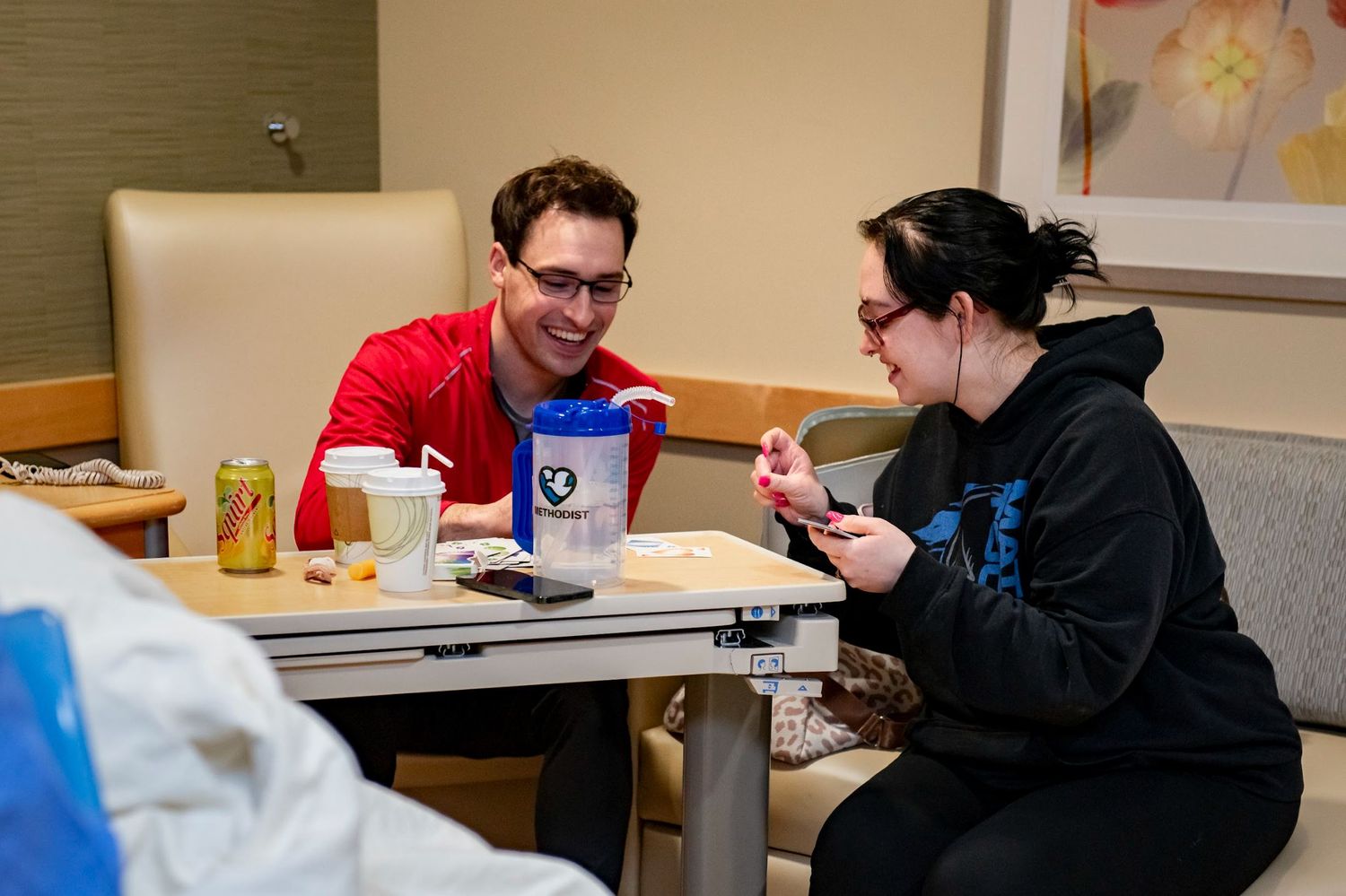 Two people share a meal at a hospital room table while having conversation