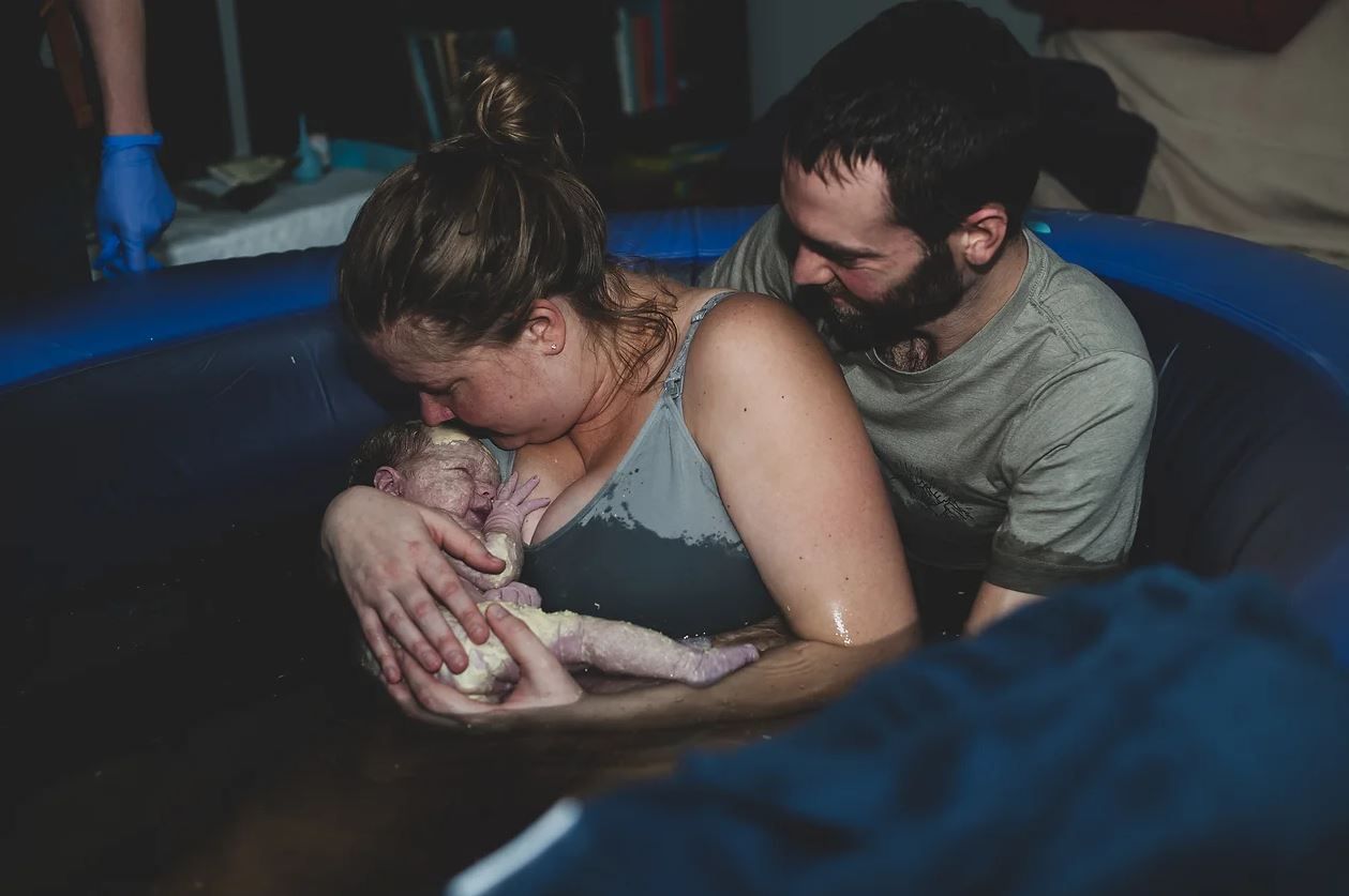 A newborn baby being held in a birthing pool during water birth.