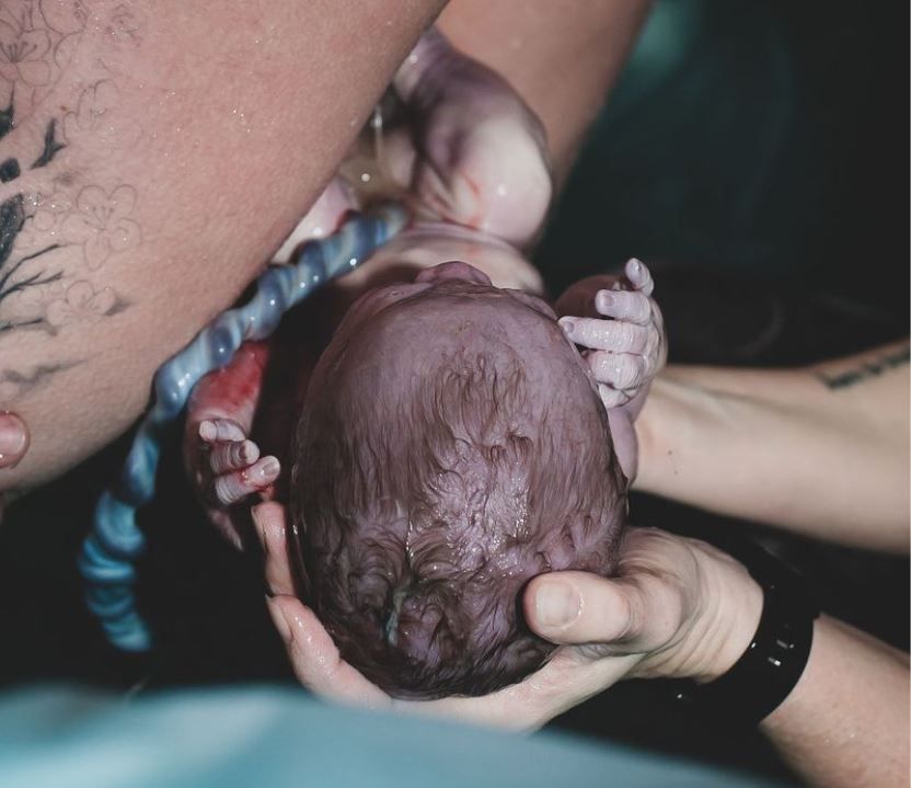 Newborn baby being gently held by multiple hands during water birth.