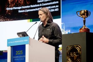 Speaker presenting at the 2025 Diggers & Dealers Mining Forum with a gold trophy displayed on stage.