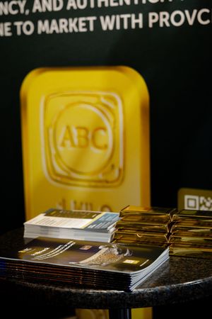 ABC Refinery gold bar display with stacked brochures on a granite table at a gold industry event.