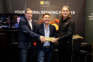 Three men holding a gold bar at the ABC Refinery Your Global Refining Partner booth.