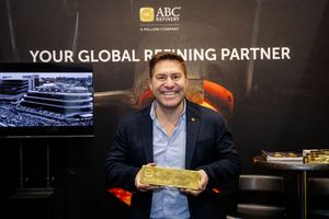 Smiling man holding a large gold bar at the ABC Refinery Your Global Refining Partner exhibit.