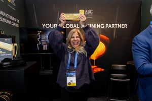 Woman triumphantly holding a gold bar at ABC Refinery Your Global Refining Partner display booth.