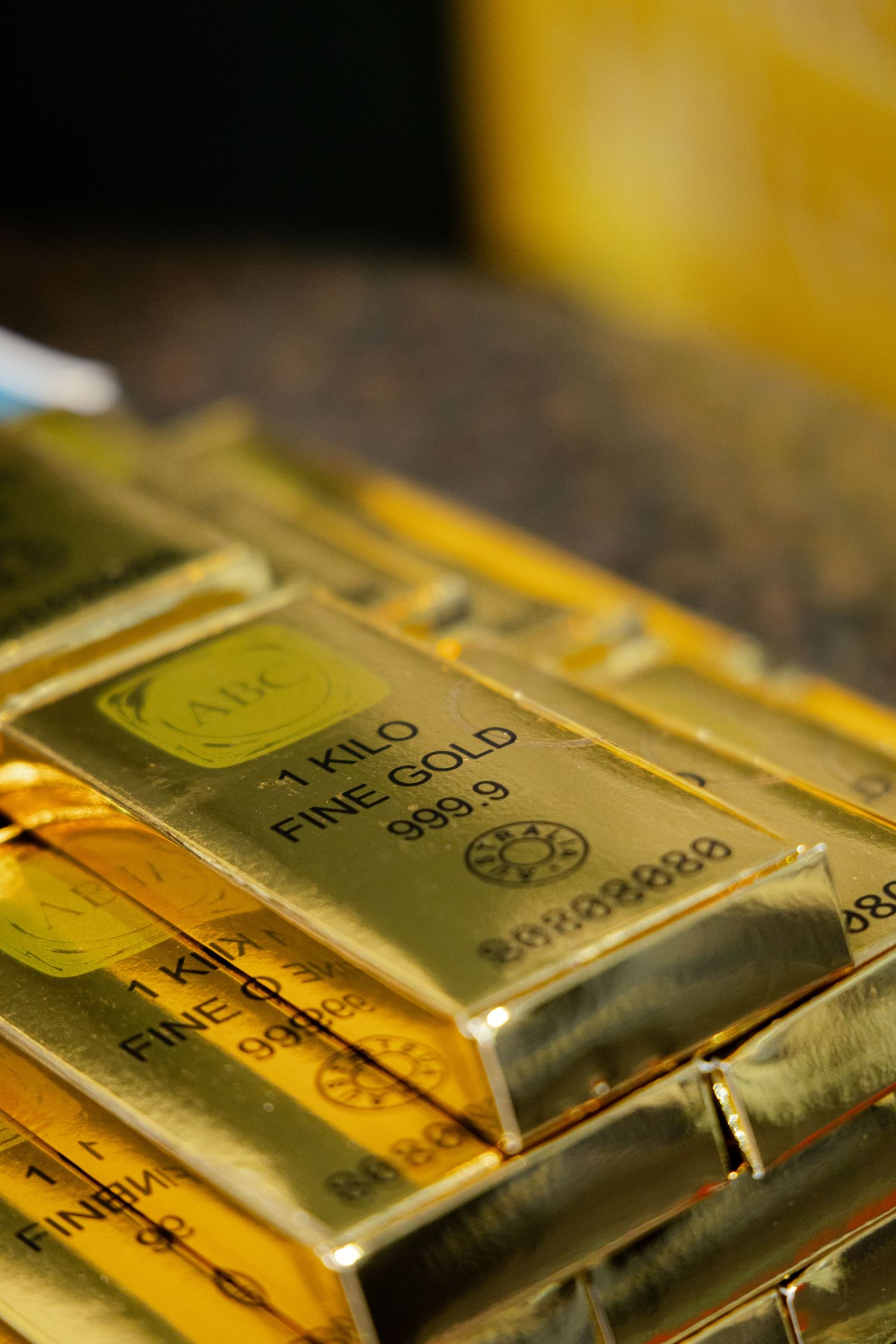 Stack of 1 kilo fine gold bars 999.9 purity with ABC hallmark stamp gleaming under warm light.