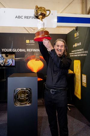 Man holding golden trophy at ABC Refinery booth at mining expo event.