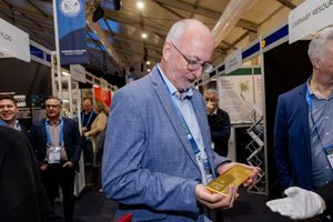 Man in blue blazer examining a gold bar at a mining industry exhibition event.