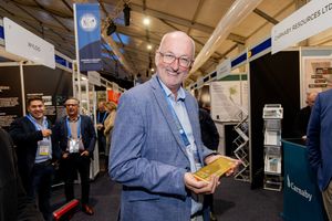 Smiling businessman holding gold bar at busy mining industry trade show exhibition.