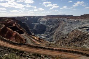 Aerial view of large open-pit gold mine with terraced walls and red dirt roads in arid landscape.