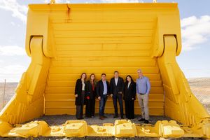 Group of six professionals standing in front of large yellow mining equipment outdoors.