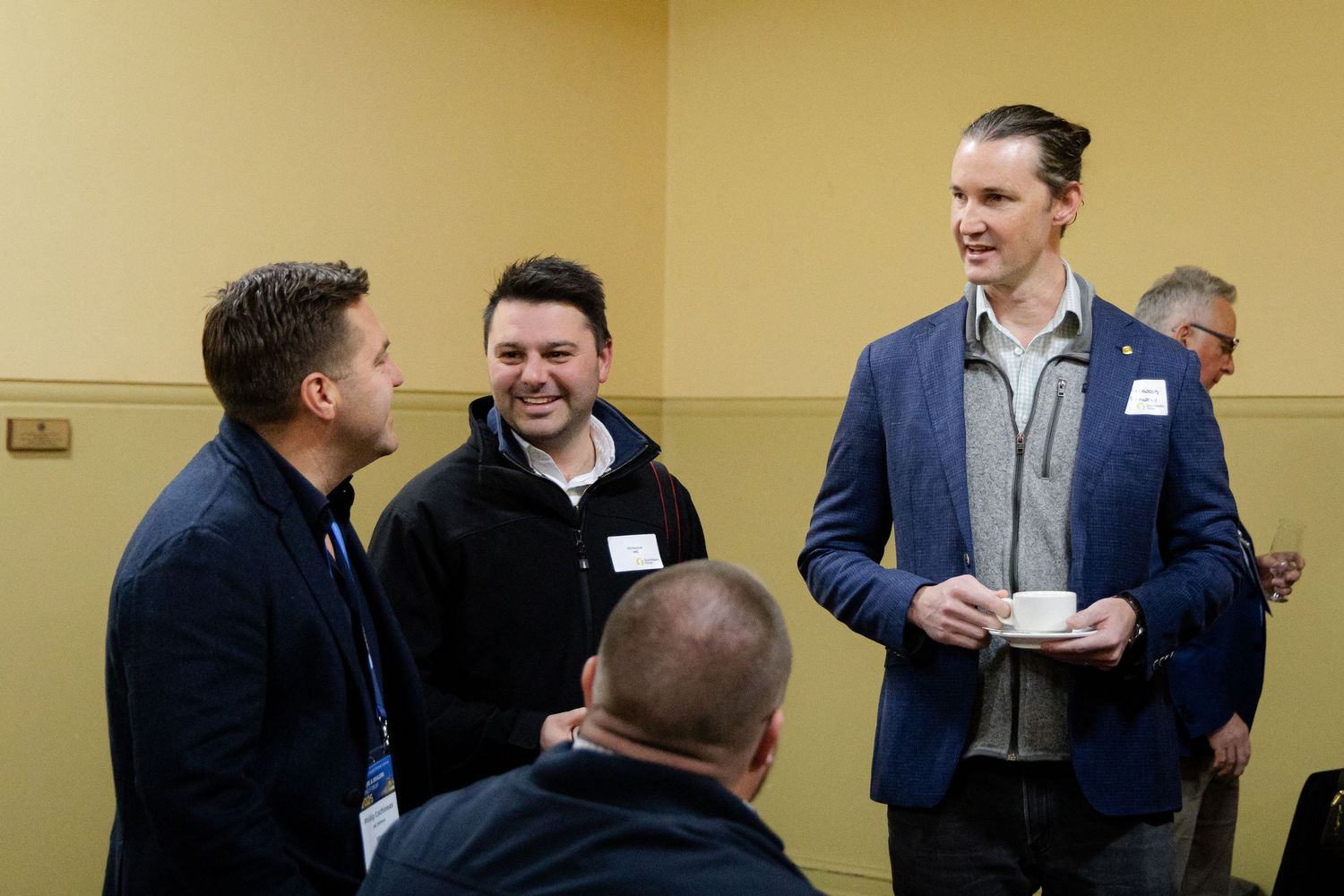Three men in smart casual attire socializing and laughing at an indoor networking event.