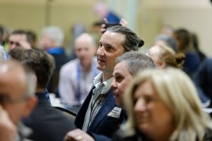 Man with hair bun attentively listening at a professional conference or business meeting event.