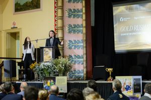 Two students presenting Gold Rush science competition results on stage at a school awards ceremony.