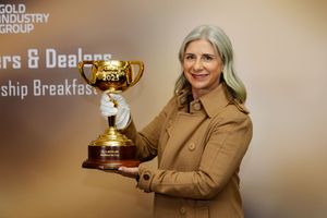 Woman in beige coat holds gold trophy cup at Gold Industry Group Diggers and Dealers Leadership Breakfast 2023.