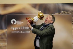 Man in green suit playfully pretends to drink from gold trophy at Diggers and Dealers Leadership Breakfast event.