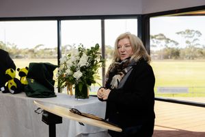 Woman standing at a table with white floral arrangement near large windows overlooking a sports field.