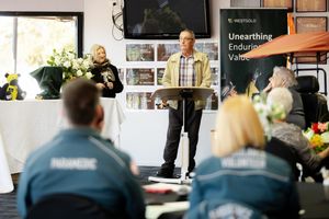 Man speaks at podium during Westgold mining presentation with paramedic and volunteer attendees seated in foreground.