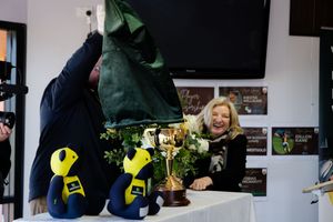 Woman laughing as a green cloth is lifted to reveal a trophy and floral arrangement at an event.