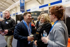 Business professionals networking and conversing at an indoor trade show exhibition event with company booths.