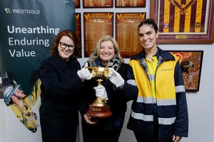 Three women holding a trophy at Westgold mining office with Unearthing Enduring Value signage.