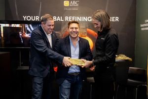 Three people smiling and holding a gold bar at ABC Refinery Your Global Refining Partner booth.