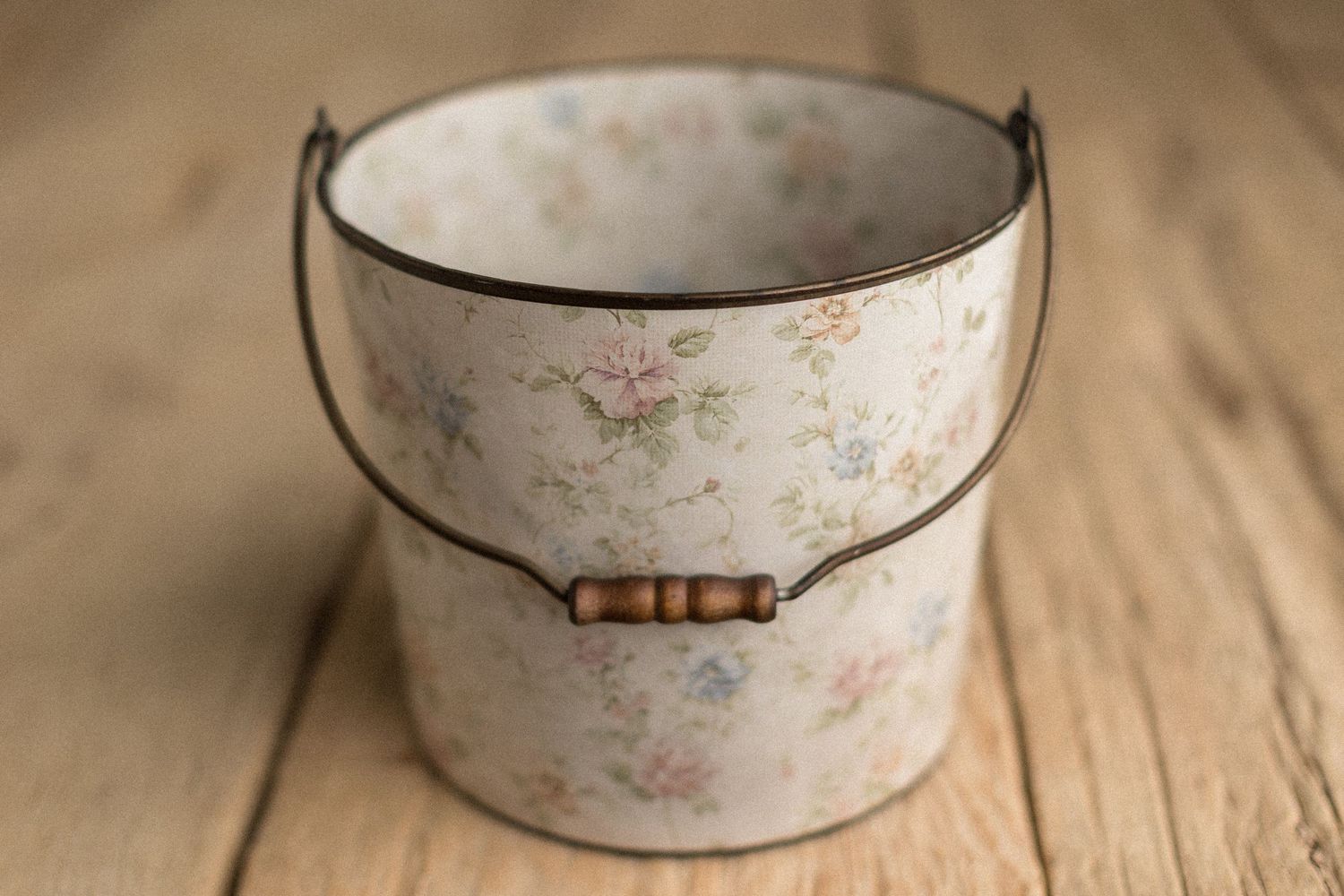 Vintage floral metal bucket with wooden handle beads on rustic wood surface.