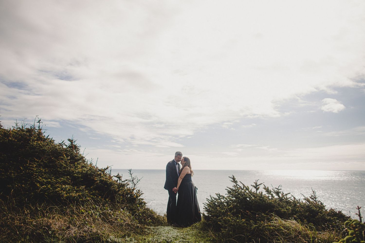 Couple in wedding attire embracing on a misty Oregon coast beach with dramatic sea stacks in the background.