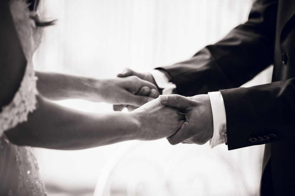Black and white photo of bride and groom exchanging rings during wedding ceremony.