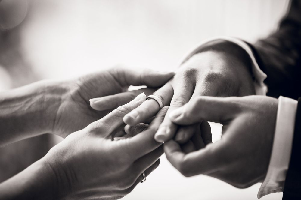 Black and white photo of a couple exchanging wedding rings during a marriage ceremony.