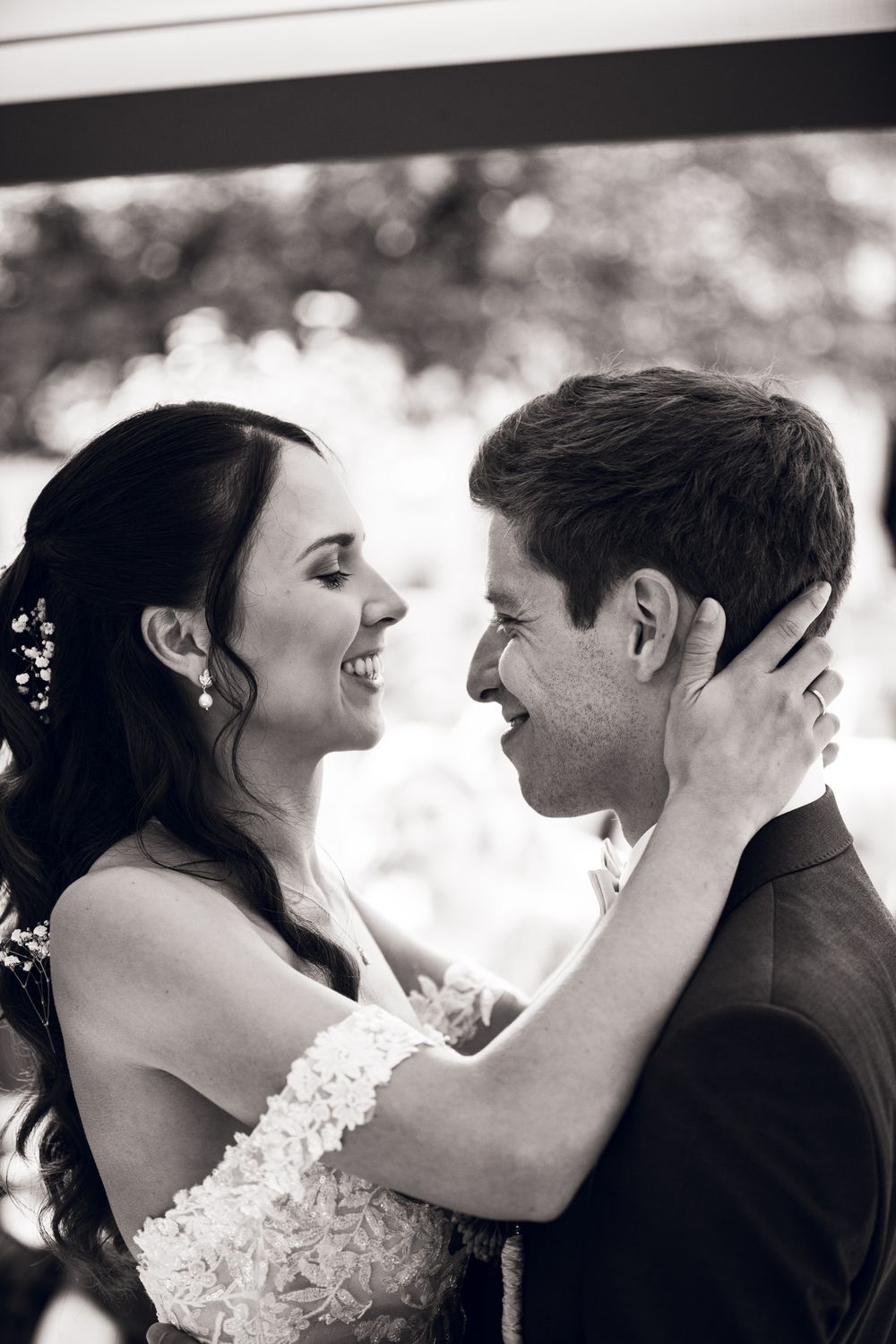 Bride and groom share a joyful intimate moment, smiling face to face on their wedding day in black and white.