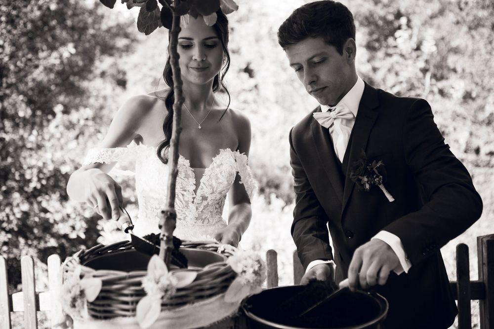 Bride and groom in elegant attire perform unity ceremony with basket outdoors in black and white.