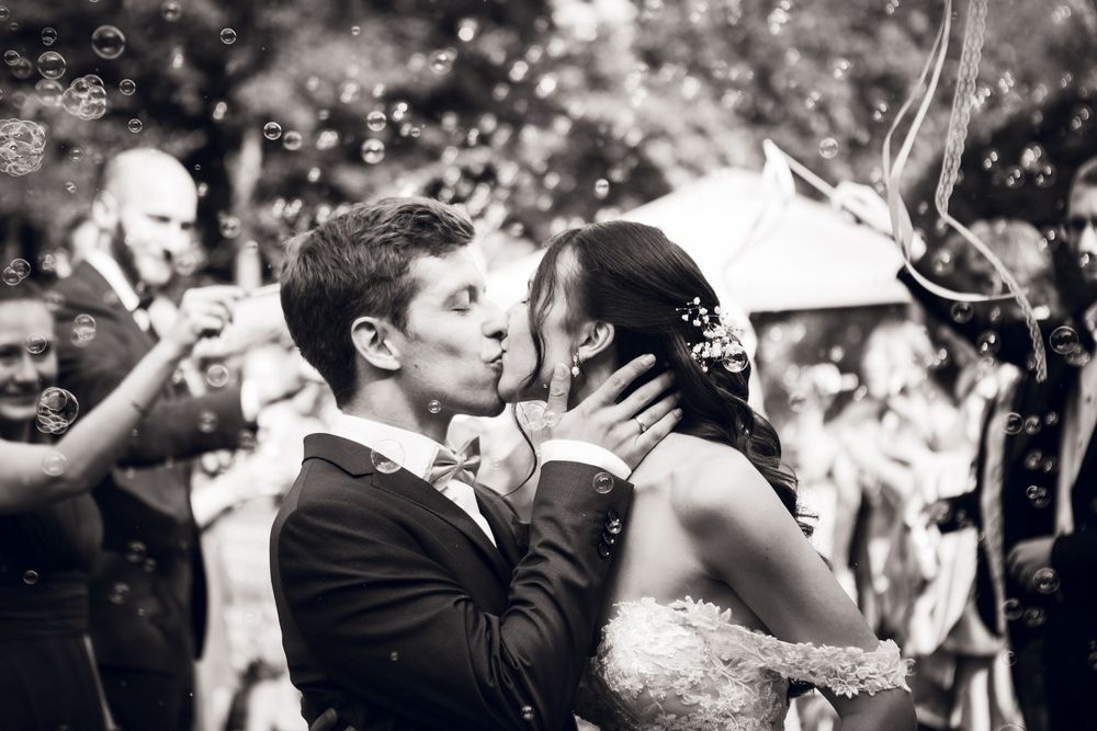 Black and white wedding photo of bride and groom sharing first kiss surrounded by bubbles.