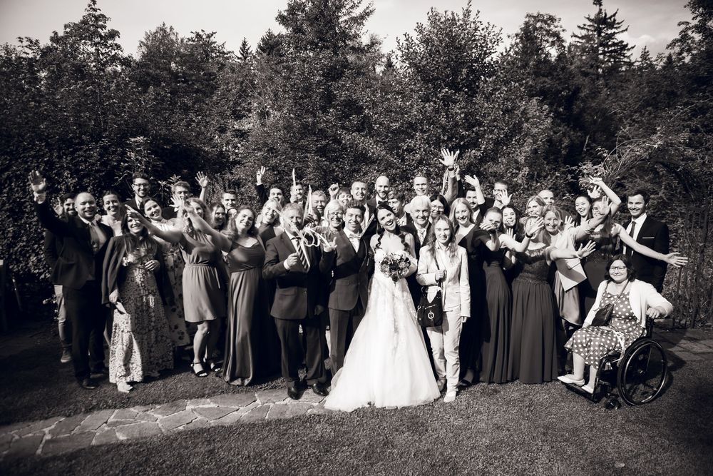 Large wedding party group photo in black and white, celebrating outdoors with raised hands.