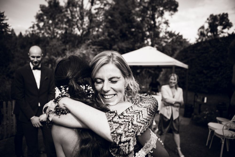 Wedding guest in sequined dress shares a warm embrace with another guest outdoors at a garden reception.
