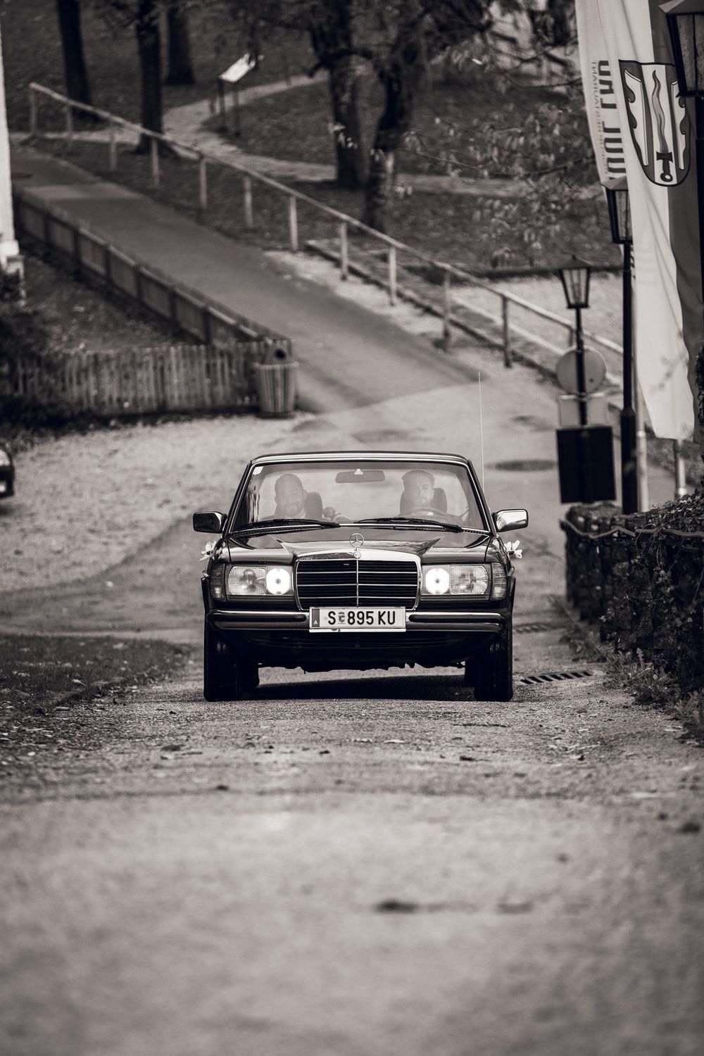 Vintage black Mercedes-Benz sedan driving on a cobblestone road in a black and white photograph.