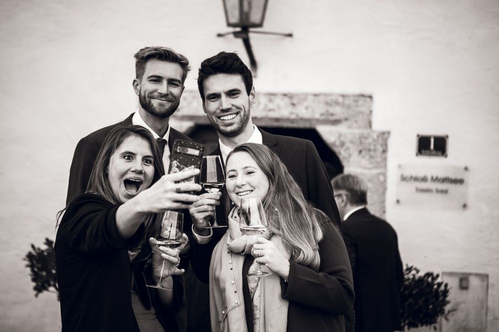 Four friends toasting with champagne glasses at an outdoor celebration in black and white photo.