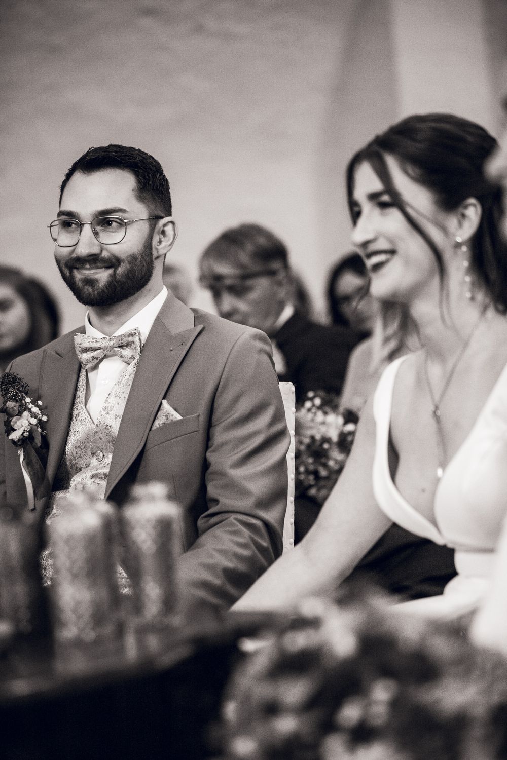 Black and white photo of smiling groom in bow tie and bride laughing together at their wedding ceremony.