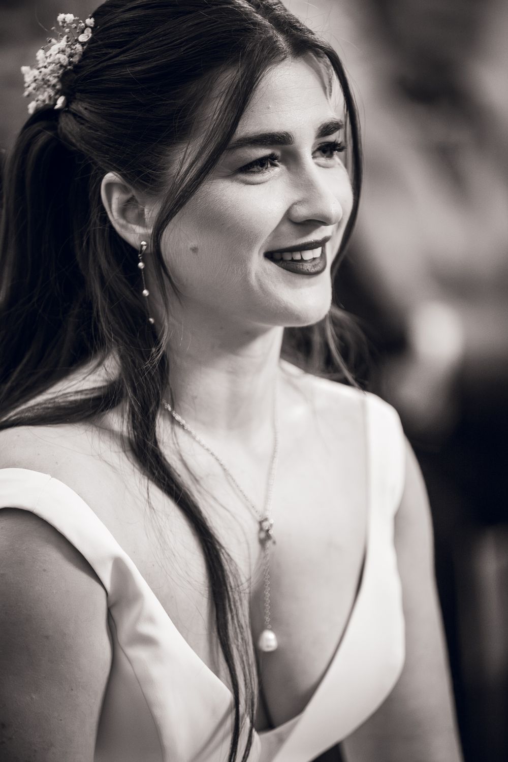 Black and white close-up portrait of a smiling bride with floral hair accessories and a pearl necklace.