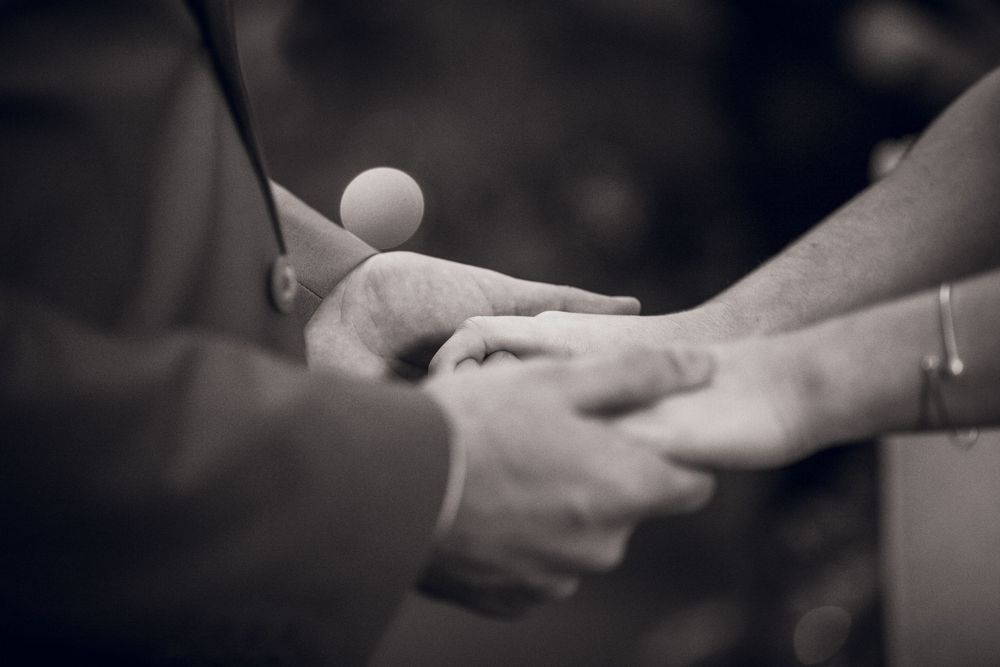 Black and white photo of two people holding hands during a wedding ceremony with a ring visible.