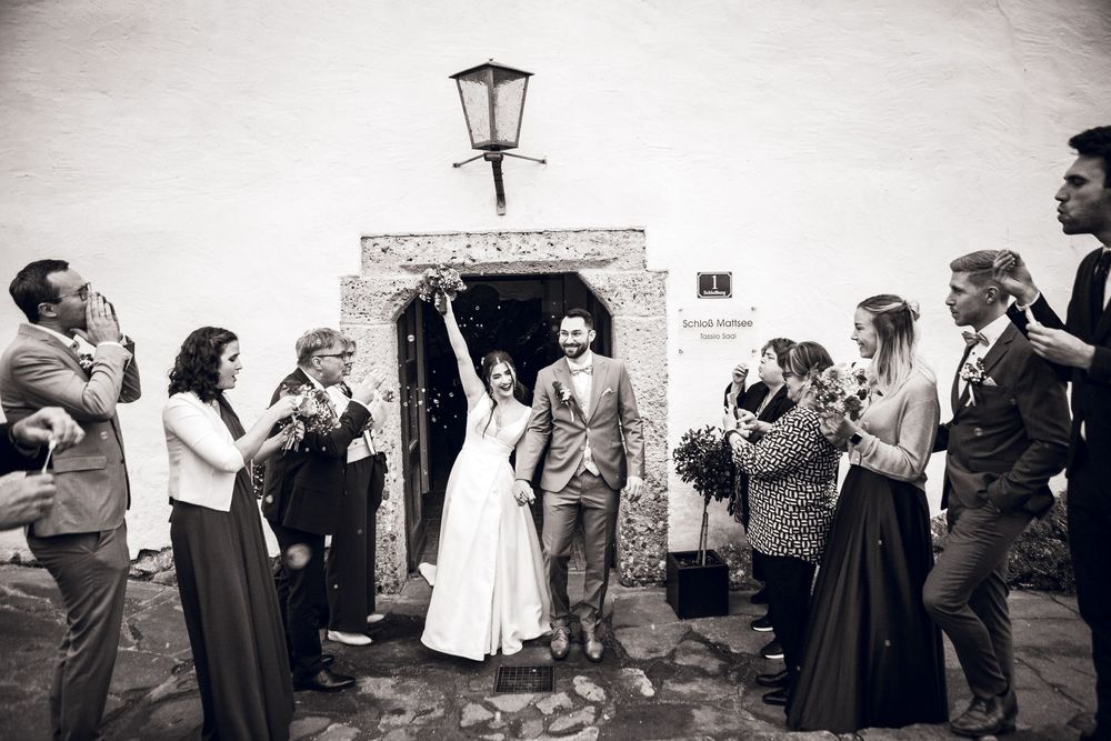 Bride and groom exit church as wedding guests celebrate with confetti in black and white photo.
