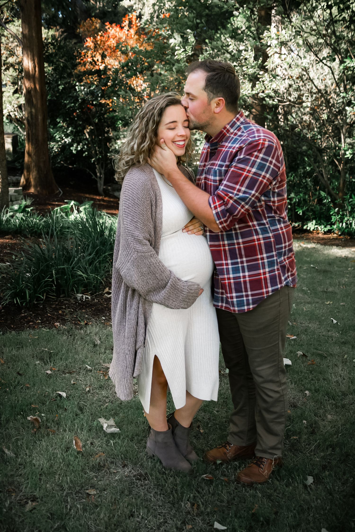 A man kisses his pregnant partner on the cheek during an outdoor maternity photo session.