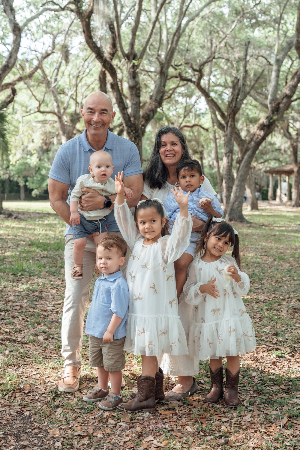 Large multigenerational family with grandparents and four young children posing and waving in a park.