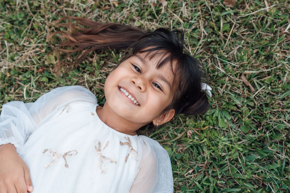 Happy young girl in white dress smiles while lying on green grass.