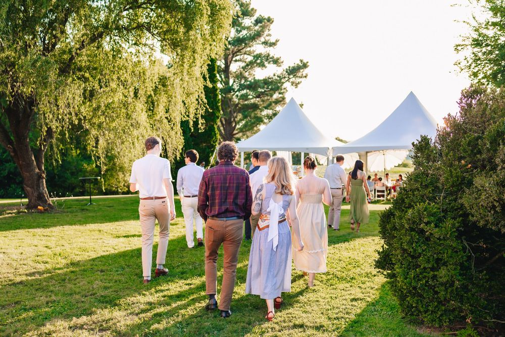 Guests walking across green lawn toward white tent at outdoor garden party event during golden hour.