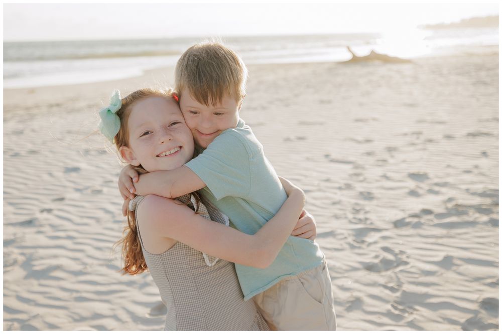 Punta Mita family photos, two siblings sharing a hug on a sandy beach with the ocean in the background.