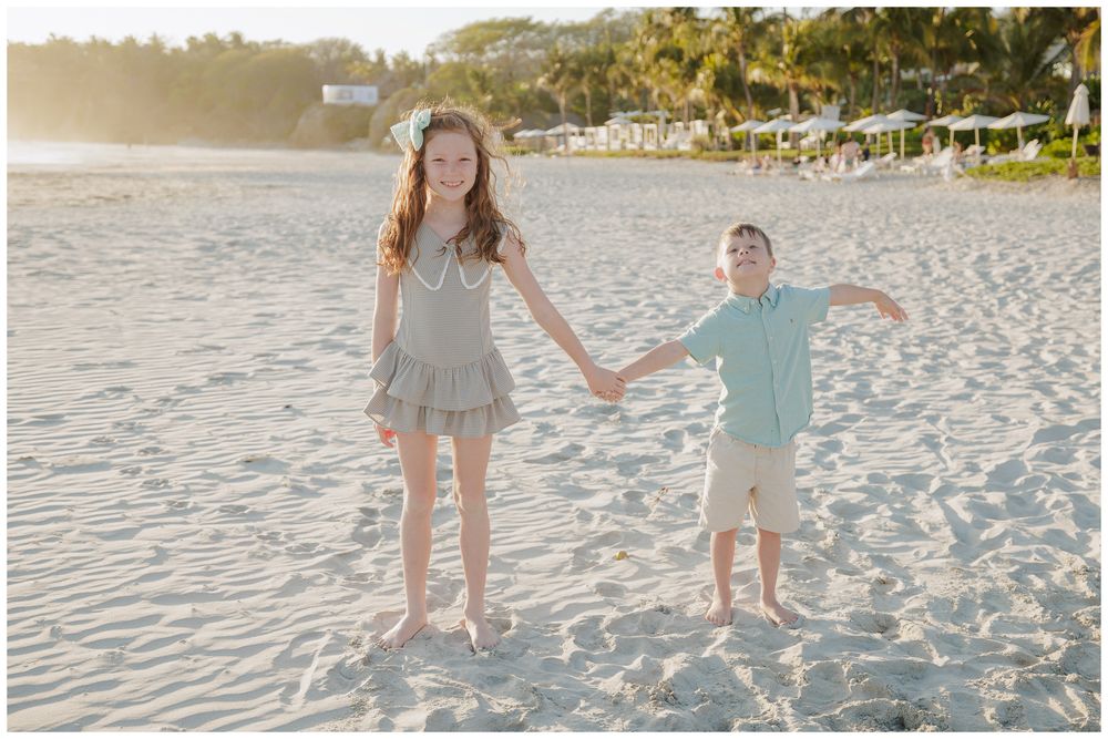 Punta Mita family photos, two children holding hands and smiling on a sandy beach during the day.