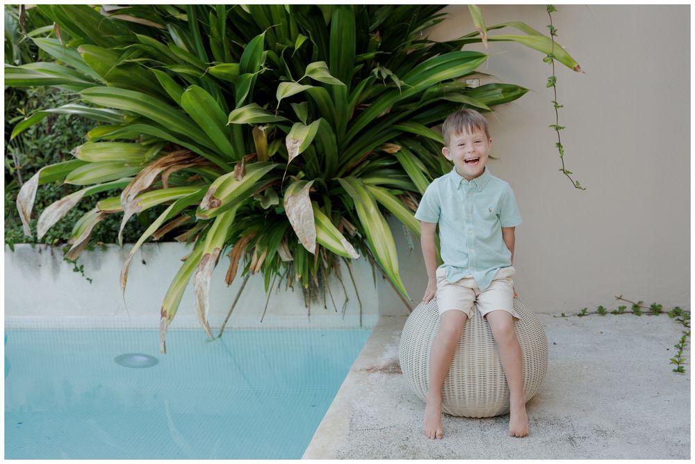 W Punta Mita family session, young boy sitting beside a pool with tropical plants in an outdoor resort setting.