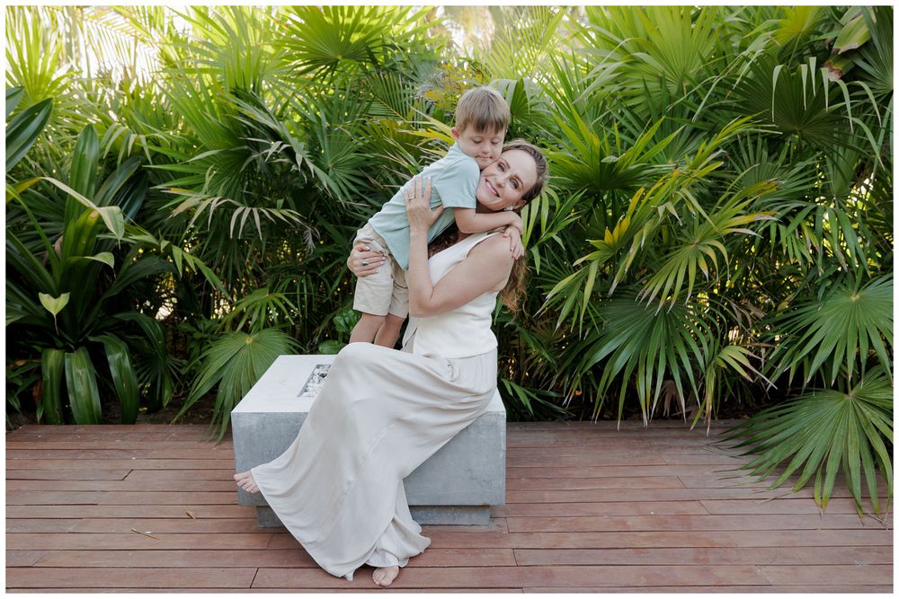 W Punta Mita family photography, mother hugging her son on a wooden deck surrounded by tropical palm greenery.